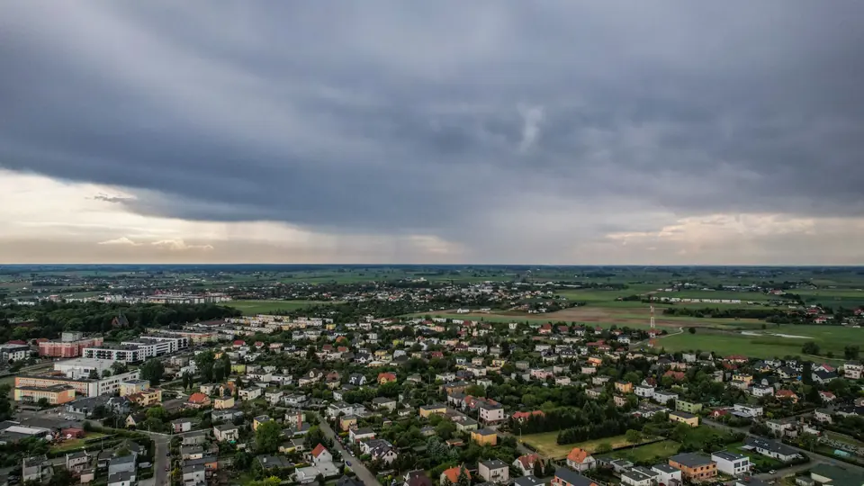 Luftaufnahme einer kleinen Landstadt mit ausgedehnten Wolken darüber und umliegenden Landschaften.