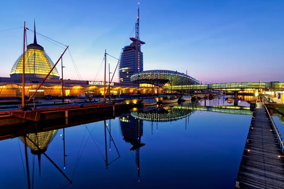 Faszinierende Dämmerungsansicht moderner beleuchteter Architektur, die sich im ruhigen Fluss in Bremerhaven, Deutschland, spiegelt.