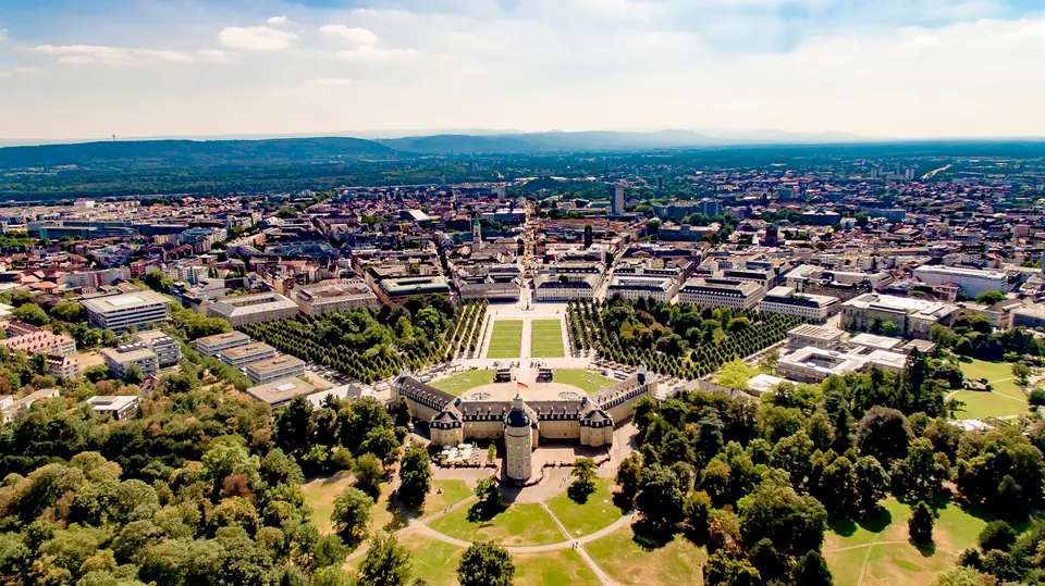 Luftaufnahme, die das Karlsruher Schloss und die umliegende Stadtlandschaft mit üppigem Grün zeigt.