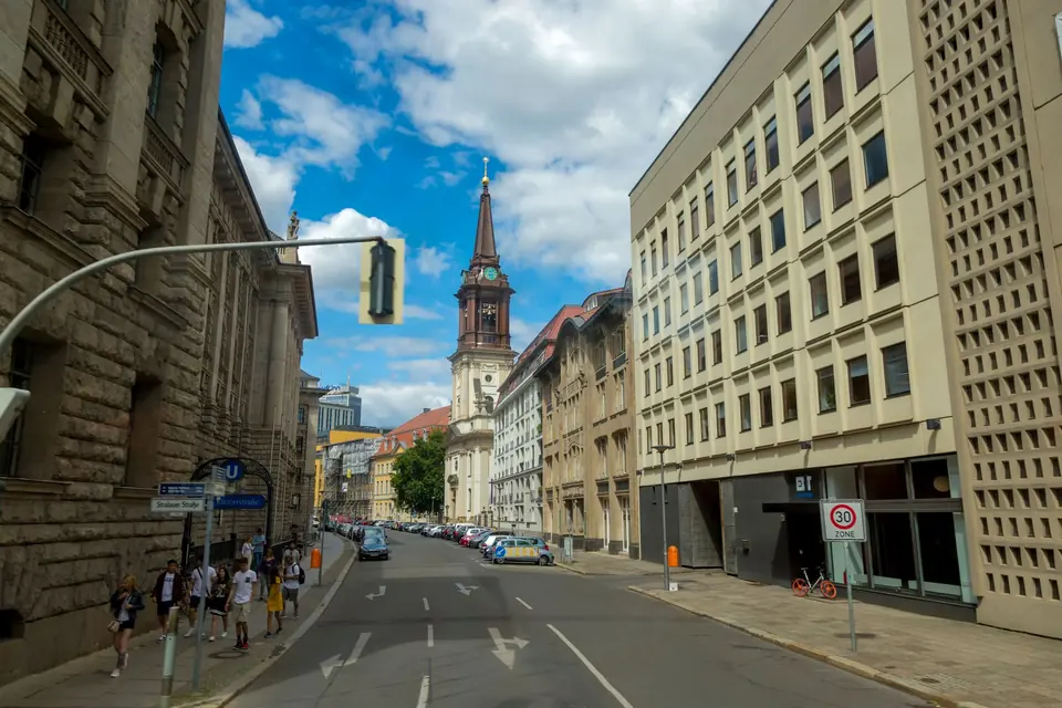 Städtische Szene einer Berliner Straße mit der historischen Marienkirche, blauem Himmel und Fußgängern.