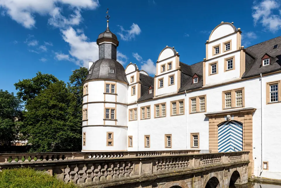 Malersicher Blick auf das Schloss Neuhaus in Paderborn, Deutschland, das seine elegante Architektur unter einem klaren blauen Himmel zeigt.