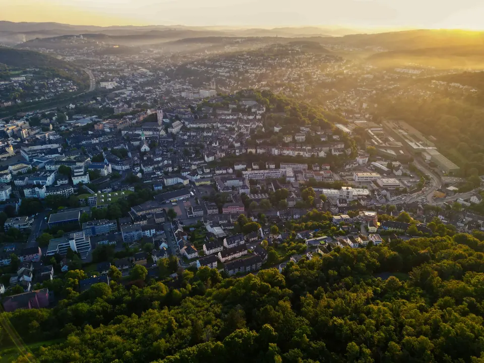 Atemberaubende Luftaufnahme von Siegen, Deutschland, gehüllt in den Sommerdämmerungsglanz, der städtische und natürliche Harmonie hervorhebt.